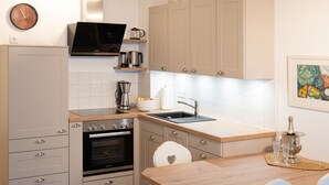 Una cocina moderna con horno empotrado, cafetera y lavaplatos. Hay una mesa de comedor de madera con sillas y un tapete decorativo.