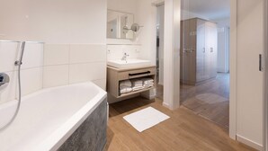 Un baño moderno con bañera, lavamanos y espejo. Cuenta con una cabina de ducha de cristal y suelo de madera.