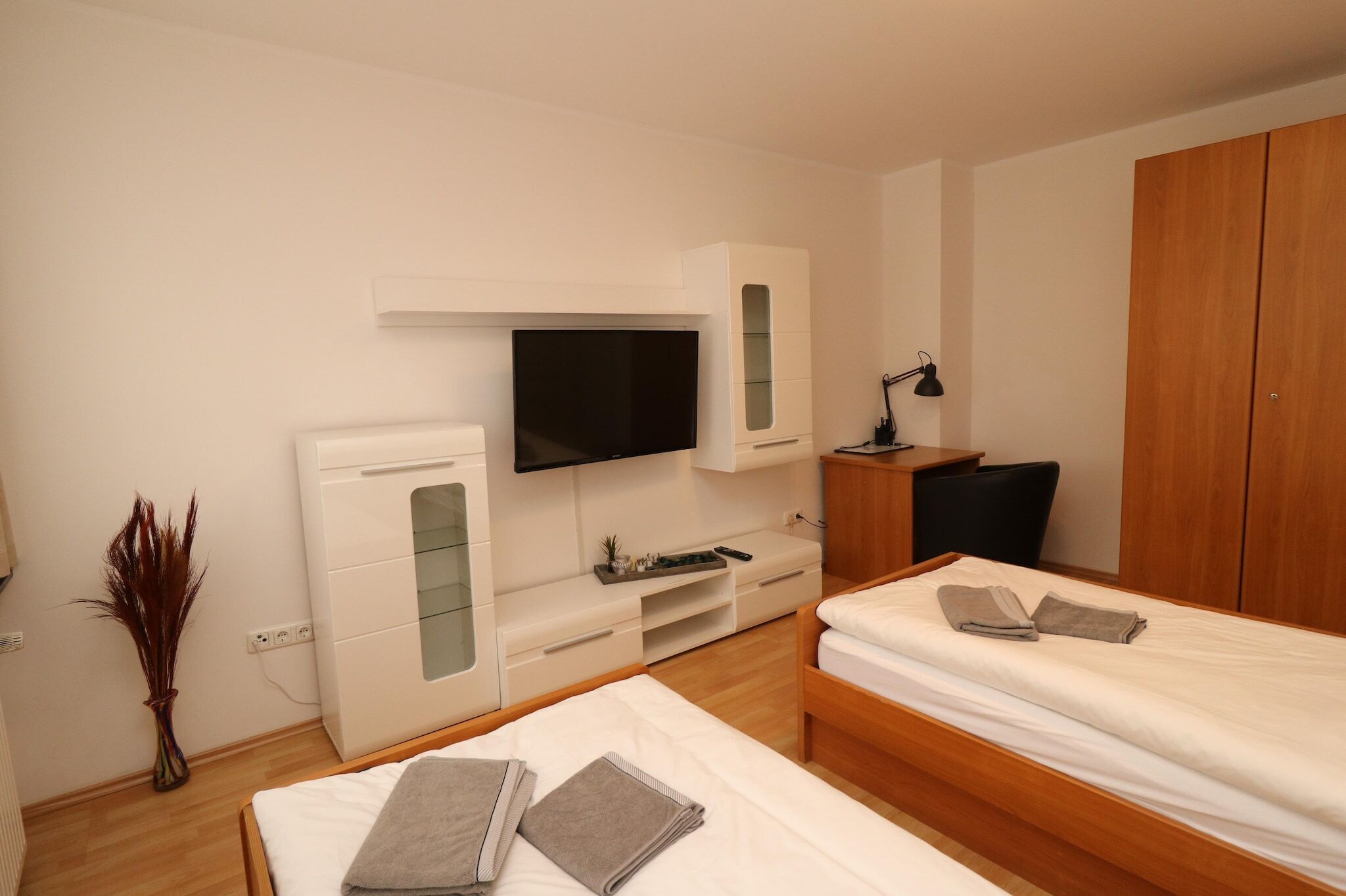 A modern hotel room with two beds, a TV, a desk, and a wardrobe.