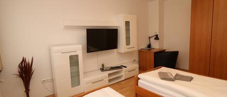 A modern hotel room with two beds, a TV, a desk, and a wardrobe.