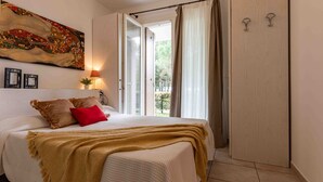 Ein Schlafzimmer mit Bett, einem Gemälde, einer Lampe und Blick ins Freie.