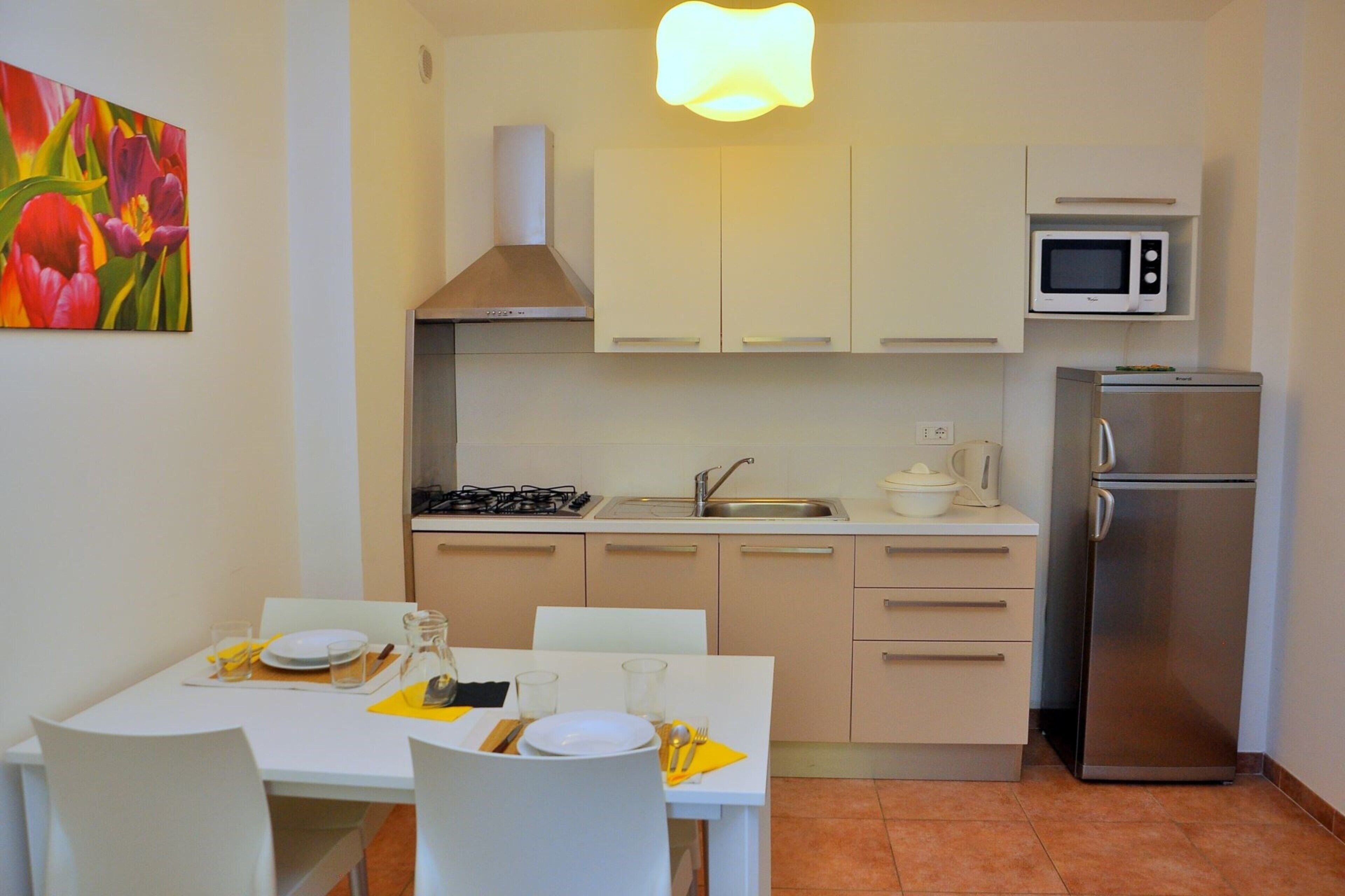 A compact kitchen with white cabinets, a stainless steel refrigerator, a microwave, and a gas stove.