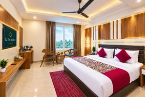 A hotel room with a bed, a desk, a chair, a ceiling fan, and a view of the outdoors. - Hotel All Time Residency - Near Connaught Place New Delhi (New Delhi)