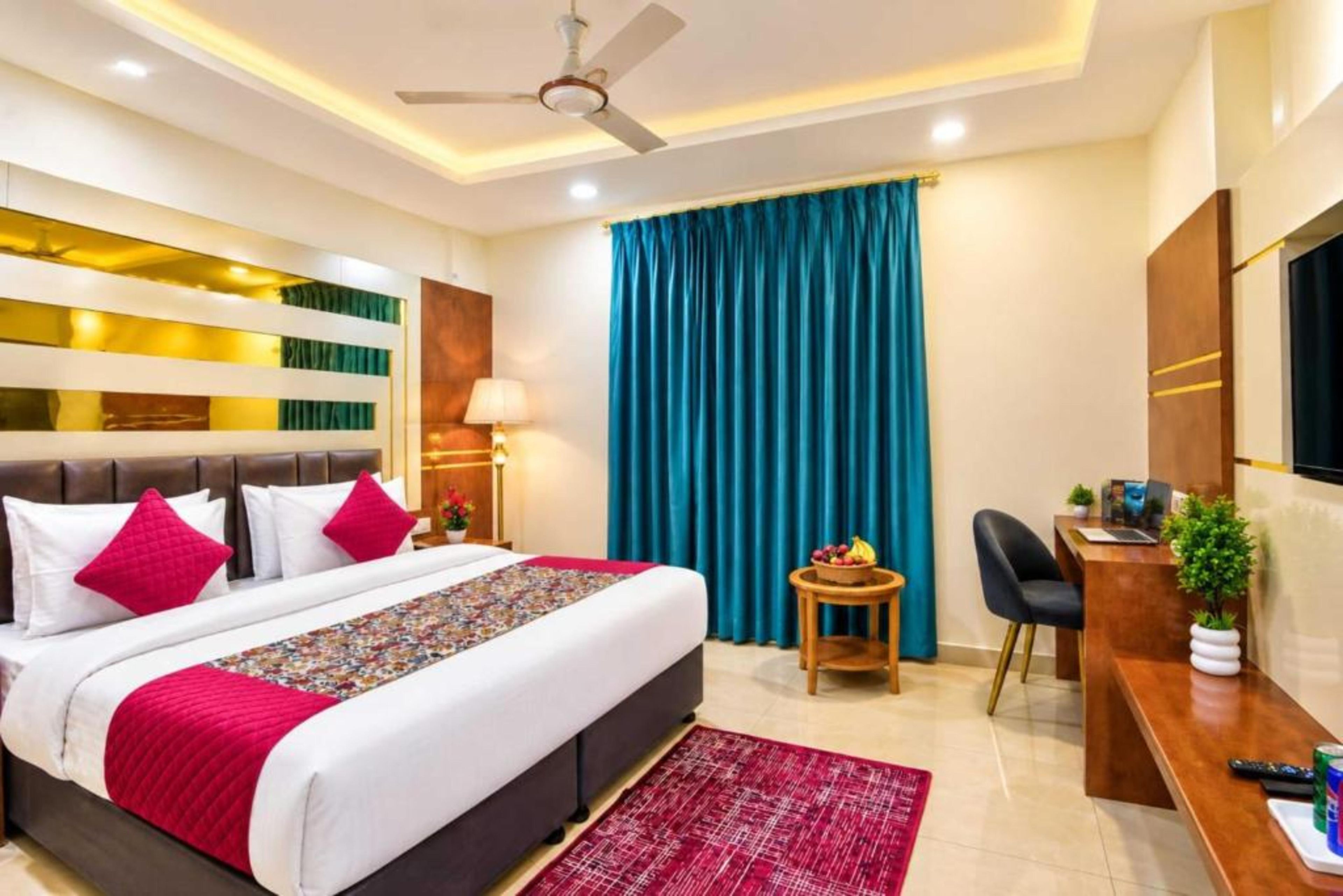 Habitación de hotel con cama, escritorio, silla, televisor y ventilador de techo.