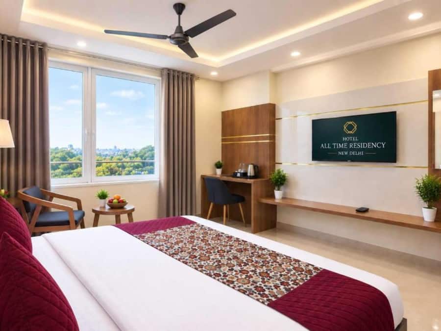 A hotel room with a bed, desk, chair, and a view of the city.