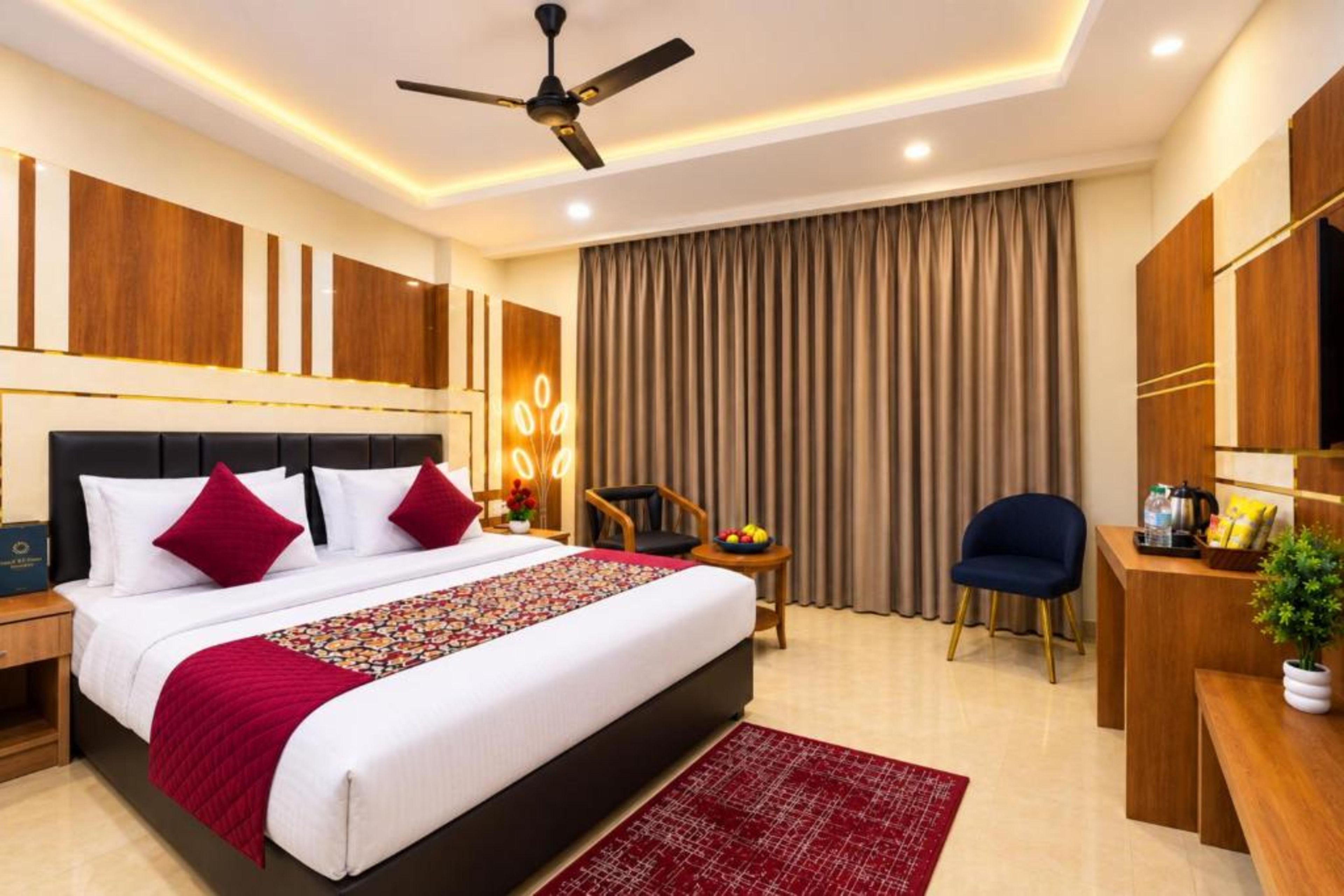 Habitación de hotel con una cama grande, un escritorio, una silla, un ventilador de techo y un ventanal con cortinas.