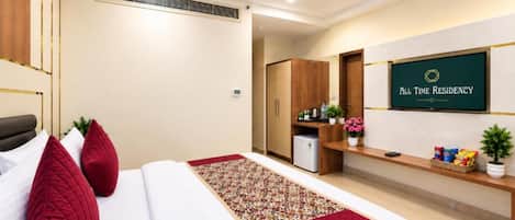 A hotel room with a bed, a desk, a refrigerator, and a television displaying 'All Time Residency'.