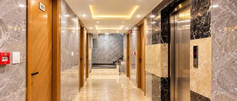 A hotel corridor with marble flooring, wooden doors, and a marble wall with an elevator.