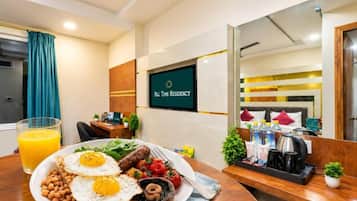 A hotel room with a dining area featuring breakfast, a TV screen with 'All Time Residency' logo, and a bed with pillows and a bedside table.