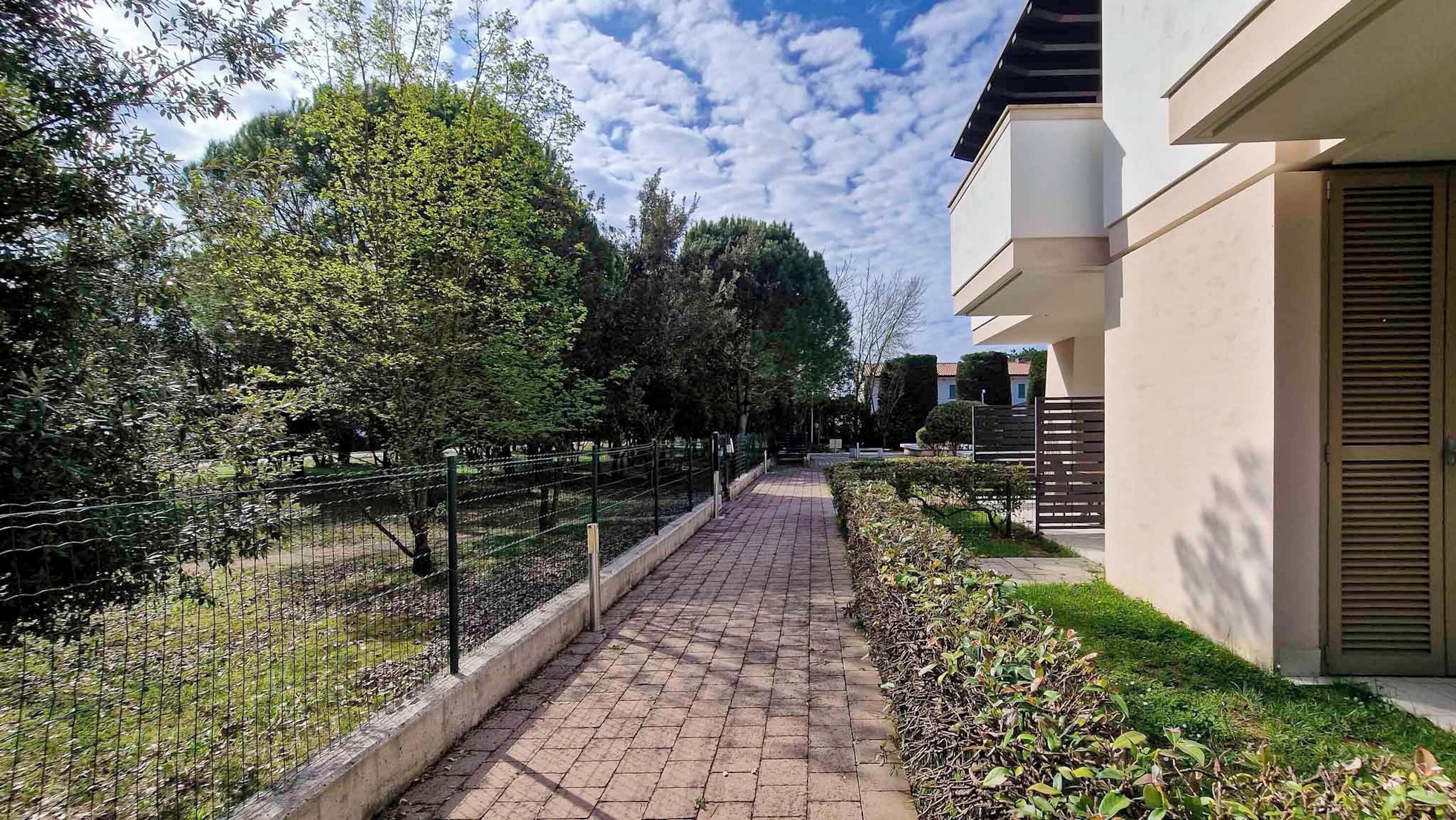 Un sendero pavimentado con una cerca de metal a un lado y un edificio con una ventana al otro.