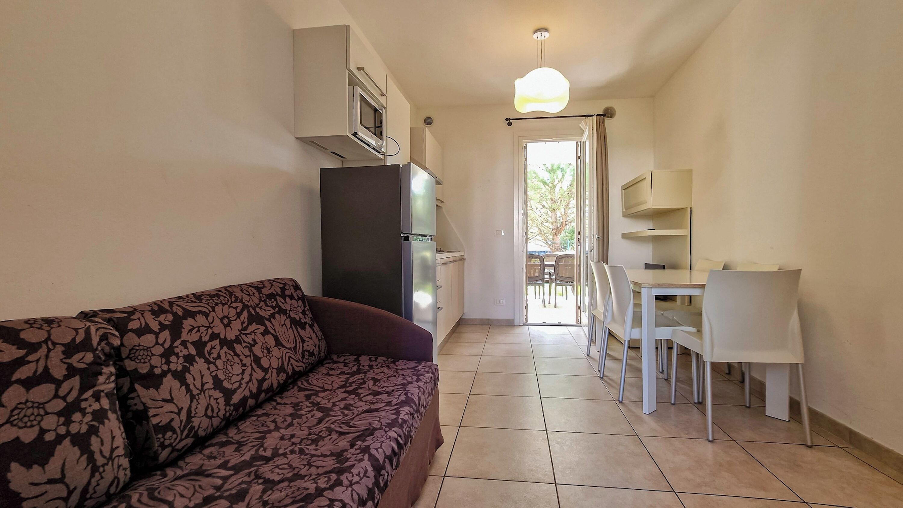 A compact living space with a sofa, a dining table with chairs, a kitchenette, and a ceiling light.