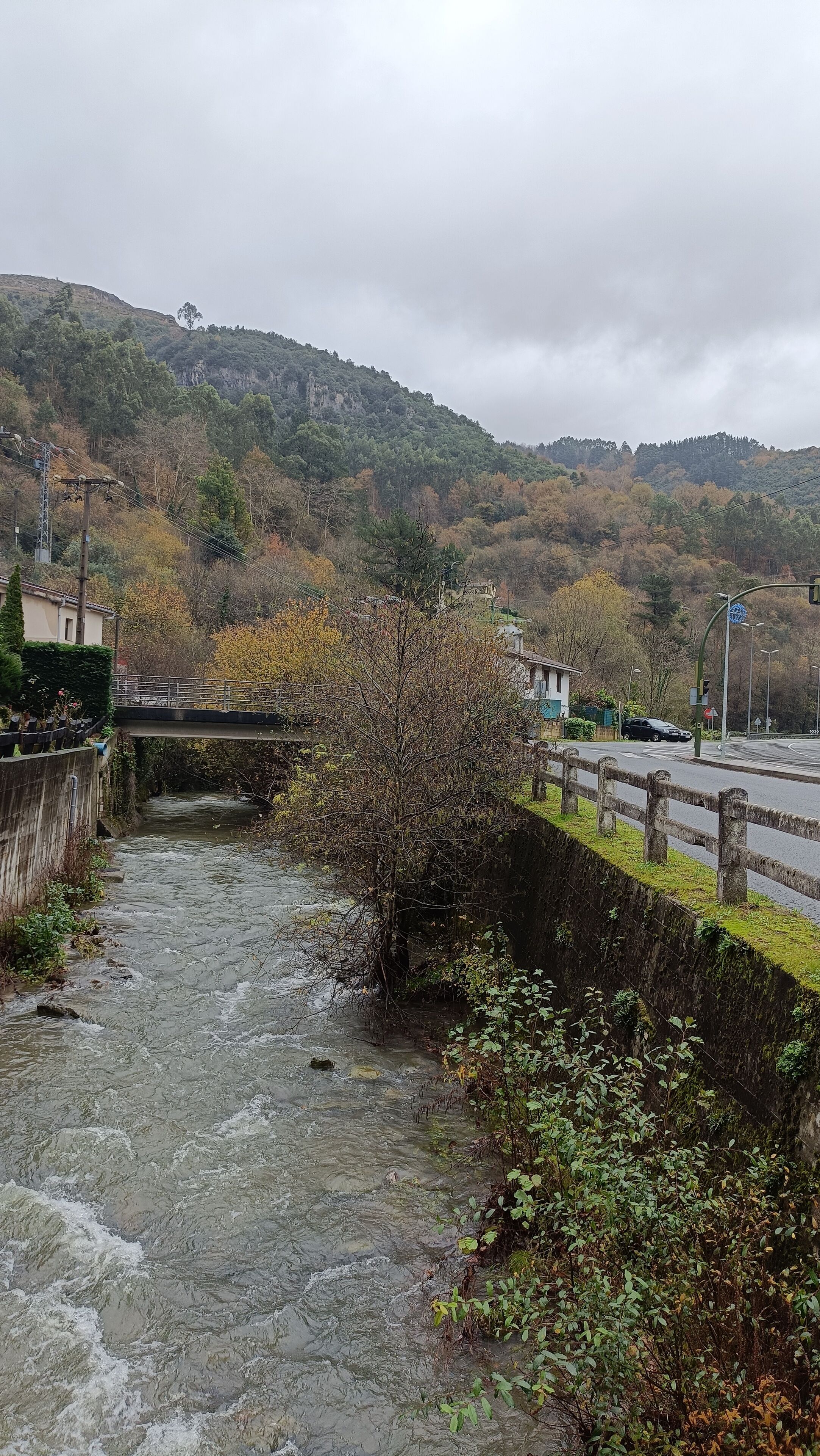 A stone bridge over a river with a view of a hilly landscape and a road with a roundabout.