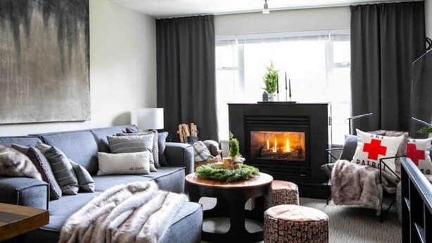 A modern living room with a fireplace, a sofa, a coffee table, and a chair with a red cross cushion.
