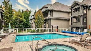 A swimming pool area with a hot tub, lounge chairs, and a view of a building with a balcony.