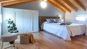 A bedroom with a bed, a nightstand, a chair, a large window, and wooden beams on the ceiling. - Chic and Stylish Apartment Facing the Pool (San Michele al Tagliamento)