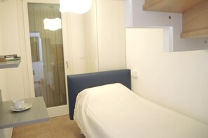 Simple, compact room with a single bed, table, and shower area, offering a functional space for a comfortable stay.