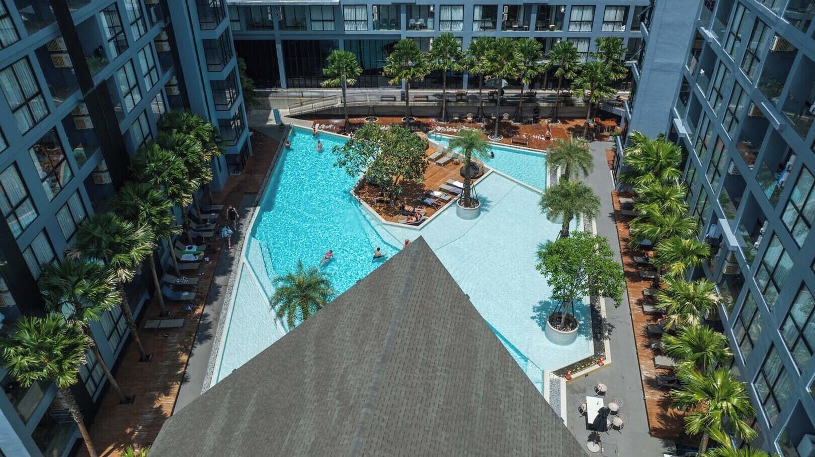Une piscine sur le toit, entourée de palmiers et de chaises longues, avec des immeubles de grande hauteur en arrière-plan.