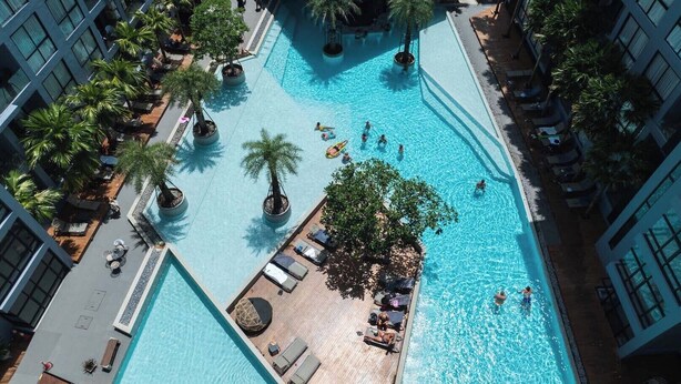 Vue aérienne d’un espace piscine d’hôtel comprenant plusieurs piscines, des chaises longues et des palmiers.
