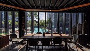 Un espace repas moderne avec une grande table et des chaises, de grandes fenêtres offrant une vue sur une piscine et la verdure environnante.