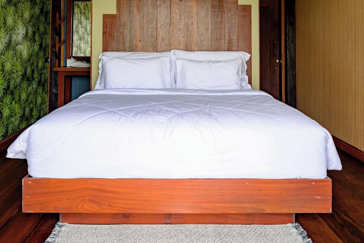 A large bed with a wooden headboard, a wooden floor, and a green wall.