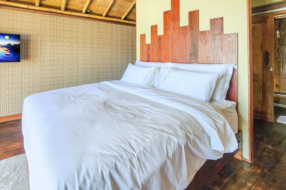 A neatly made bed with white linens in a room with a bamboo wall and a wooden headboard.