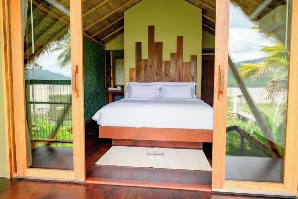 Une chambre avec un lit en bois, un mur vert et une vue sur l’extérieur.
