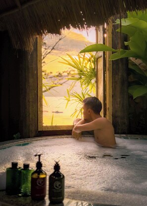 Una persona en una bañera con vista a un atardecer a través de una ventana.
