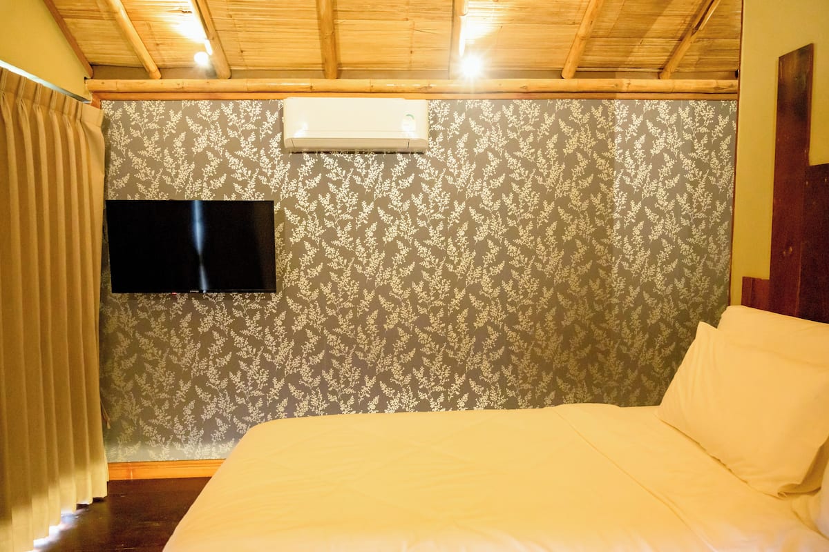 A bedroom with a bed, a flat-screen TV mounted on the wall, and a patterned wallpaper.