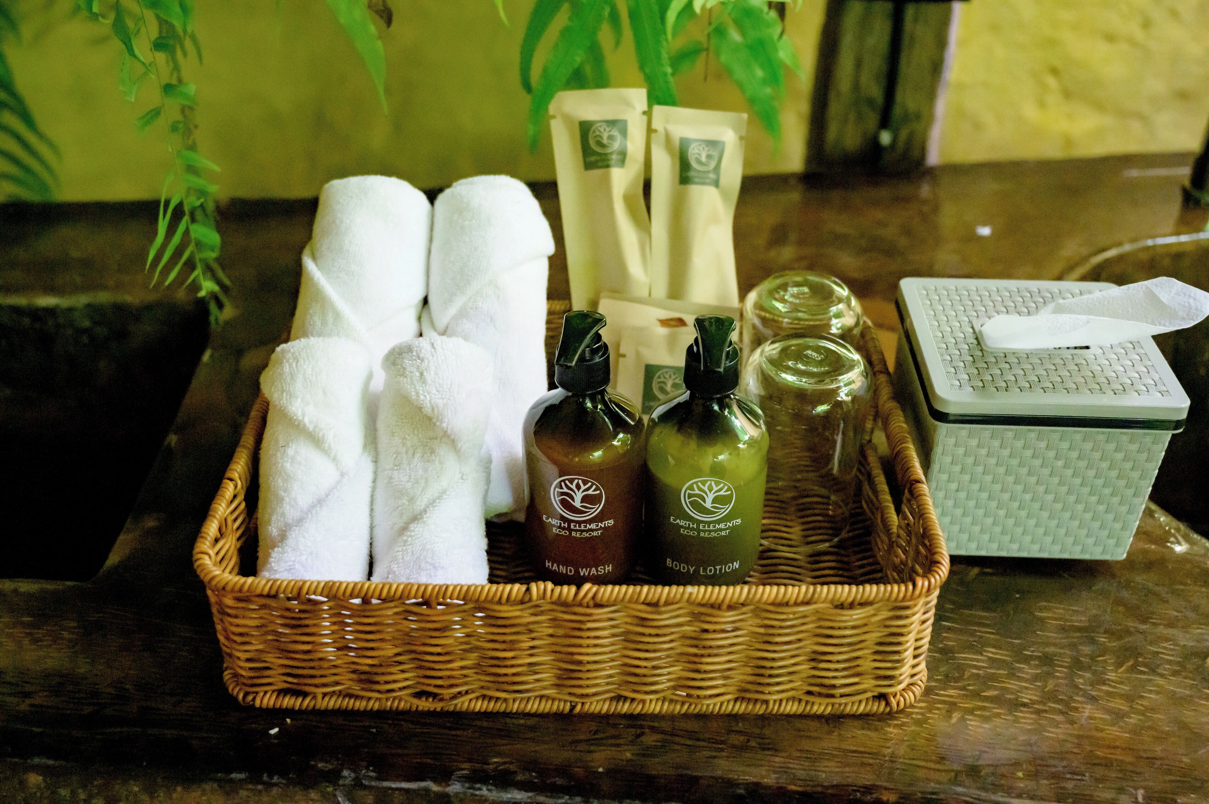 A wicker basket containing towels, two bottles of body lotion, and a tissue box on a wooden surface.