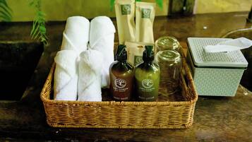 A wicker basket containing towels, two bottles of body lotion, and a tissue box on a wooden surface.