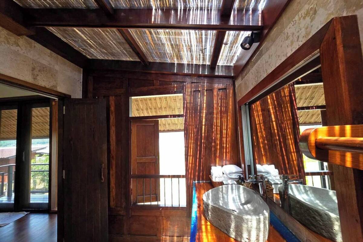 A bathroom with a large mirror, a stone sink, and a wooden door leading to a balcony.