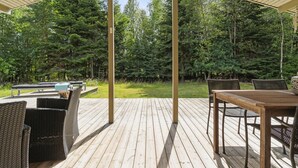 A wooden deck with outdoor furniture, including a table and chairs, overlooking a forested area.