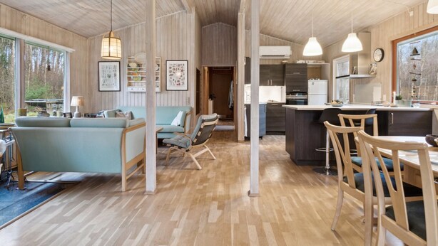 A spacious living area with a sofa, chairs, and a dining table. There is a kitchen area with a refrigerator and a sink.