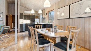 A modern kitchen with wooden cabinets, a dining table with chairs, pendant lights, and framed maps on the wall.