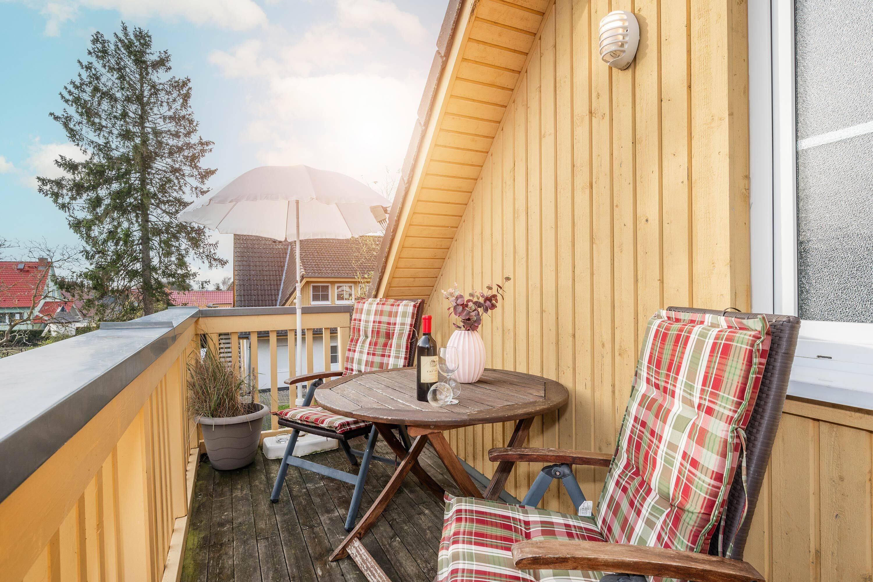 Eine Holzterrasse mit einem runden Tisch, zwei Stühlen, einem Blumentopf und einer Weinflasche.