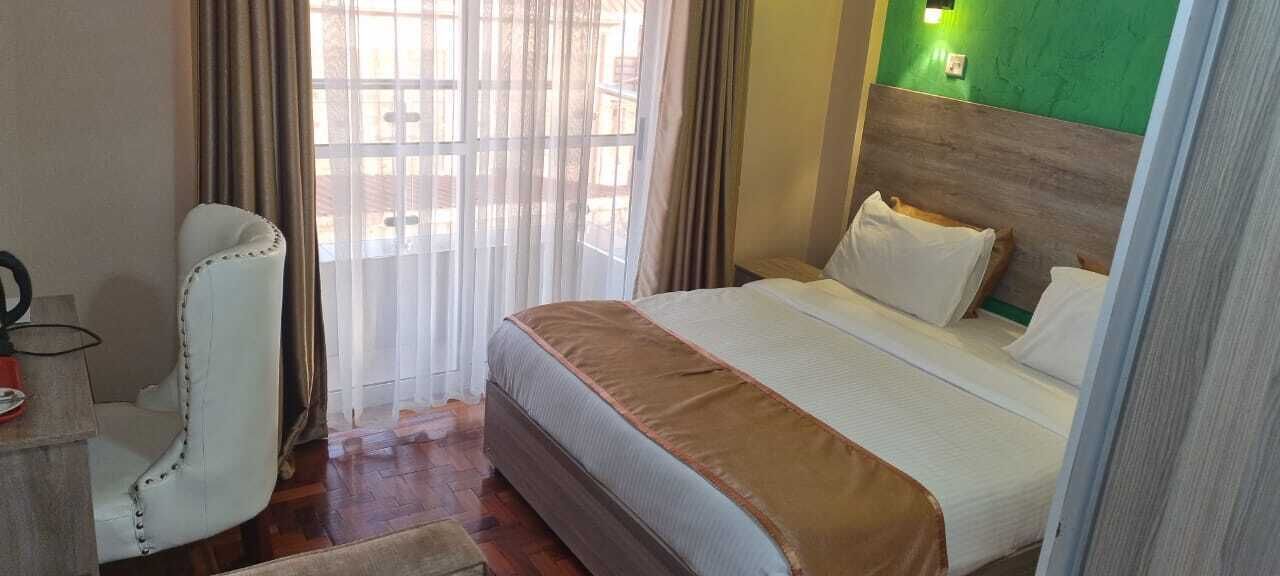 Una camera d'albergo con un letto, una sedia, una scrivania e una finestra con tende.
