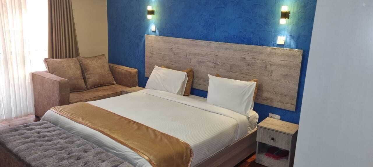 A hotel room with a large bed, a wooden headboard, two bedside tables, a sofa, and a window with curtains.