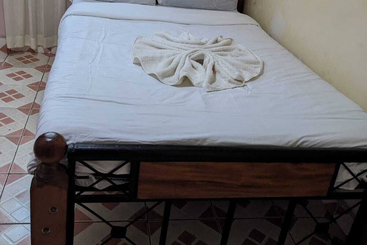 A neatly made bed with a towel on it, a wooden headboard, and a patterned floor.
