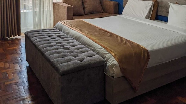 A modern hotel room with a large bed, a bench, and a view of the outside through sheer curtains. - Essence Hotel (Ndenderu)
