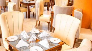 A dining area with tables set for four, each with white plates, cutlery, and glasses. - Essence Hotel (Ndenderu)
