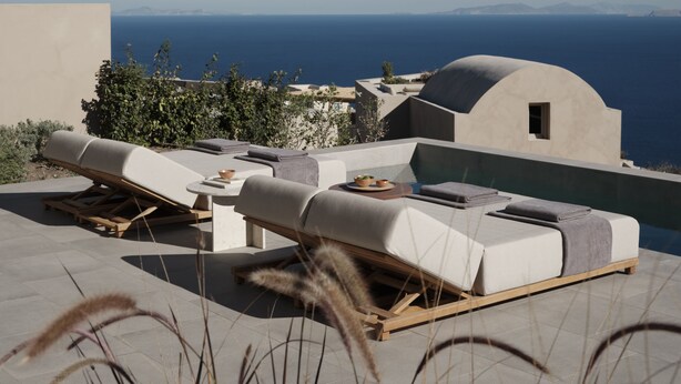 A rooftop terrace with lounge chairs, a table, and a view of the sea and distant mountains.