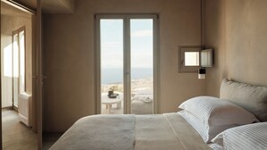 A bedroom with a bed, a view of the sea through a sliding door, and a small table with a chair outside.