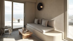 A modern living room with a sofa, a coffee table, and a view of the sea through large windows.