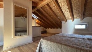 A bedroom with a sloped ceiling, wooden beams, a large bed, a window, and a built-in bench. - Stunning Apartment With Shared Pool (San Michele al Tagliamento)