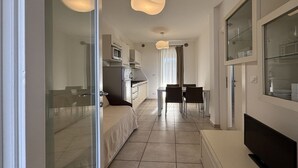 A modern, well-lit hotel room with a glass door leading to a balcony, a dining area with a table and chairs, and a TV on the right side. - Stunning Apartment With Shared Pool (San Michele al Tagliamento)