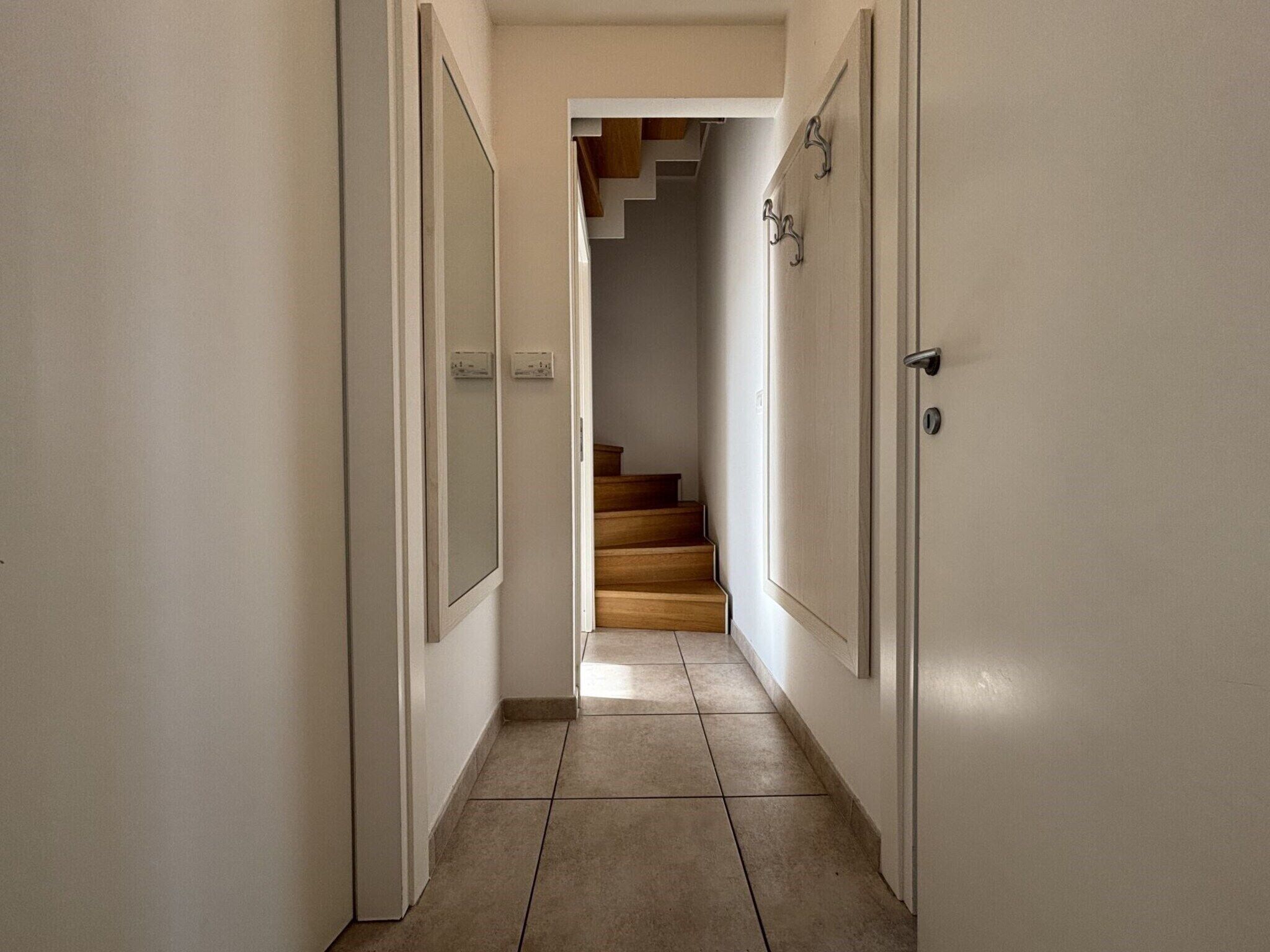 A narrow hallway with a wooden staircase leading to a landing.
