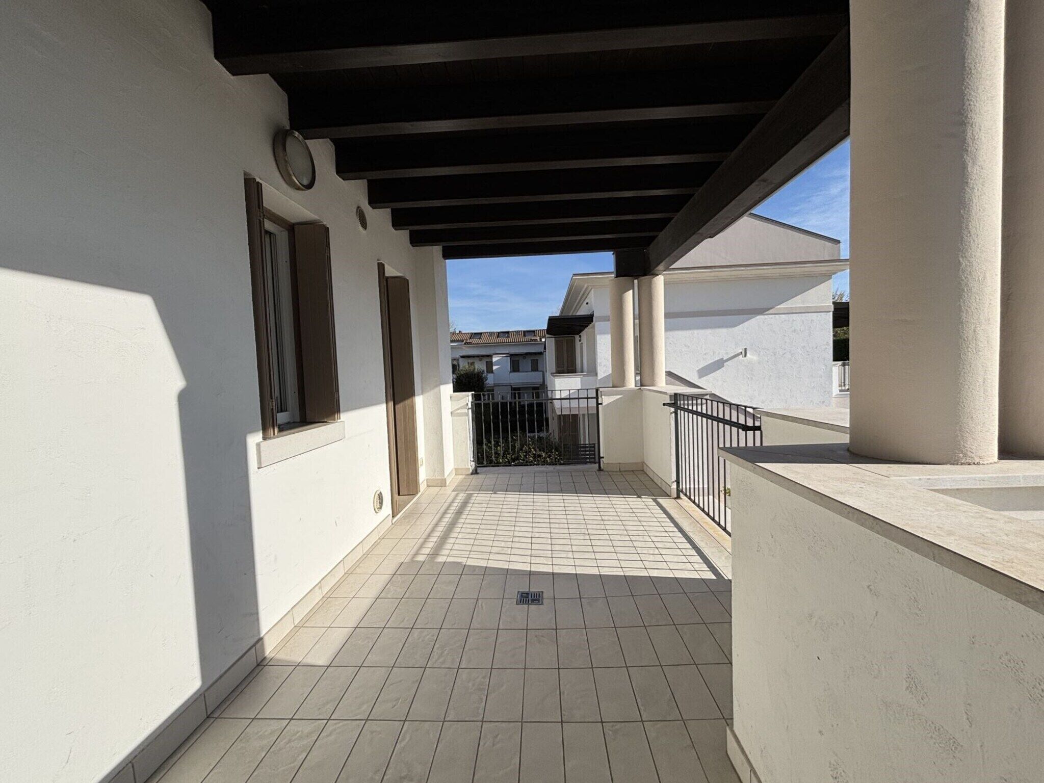 A covered outdoor corridor with tiled flooring, a metal railing, and a view of neighboring buildings.