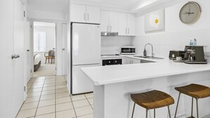 A modern kitchen with white cabinetry, a refrigerator, a microwave, a coffee machine, and a large island with stools. - Lindy Lou's Entire Rental Unit in Sawtell (SAWTELL)