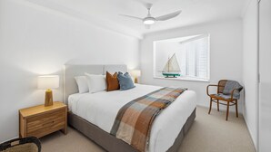 A bedroom with a bed, nightstands, a chair, a ceiling fan, and a window with blinds. - Lindy Lou's Entire Rental Unit in Sawtell (SAWTELL)
