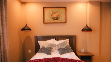 A neatly made bed with a red blanket, two black lamps, and a painting on the wall.